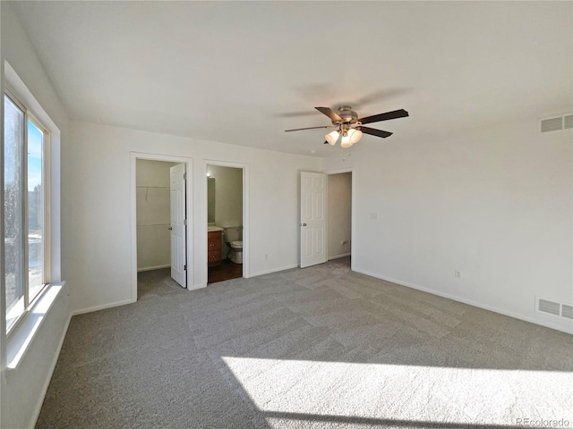 unfurnished bedroom with ceiling fan, multiple windows, connected bathroom, a spacious closet, and a closet