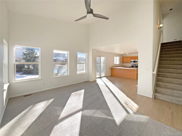 carpeted living room with a towering ceiling, a wealth of natural light, and ceiling fan