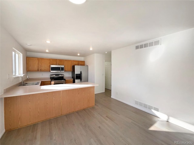 kitchen featuring appliances with stainless steel finishes, sink, light wood-type flooring, and kitchen peninsula