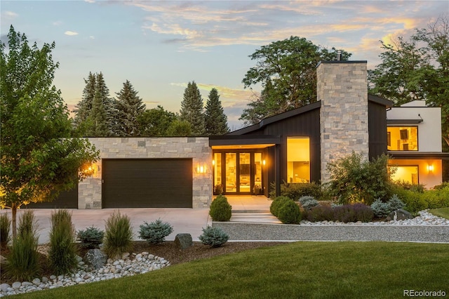 contemporary home with driveway, stone siding, a front yard, a garage, and a chimney