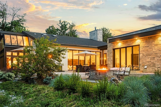 back of property featuring a patio area, stone siding, a chimney, and a fire pit