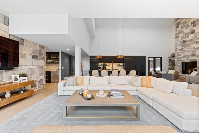 living area with a high ceiling, a stone fireplace, and wood finished floors