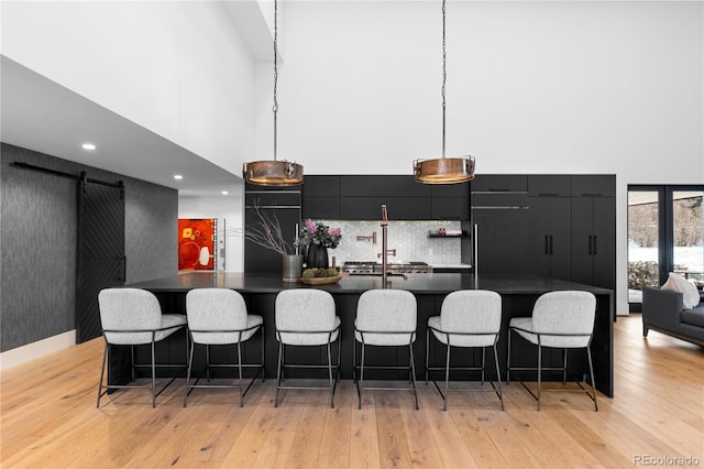 kitchen with light wood-type flooring, modern cabinets, dark countertops, a barn door, and dark cabinets