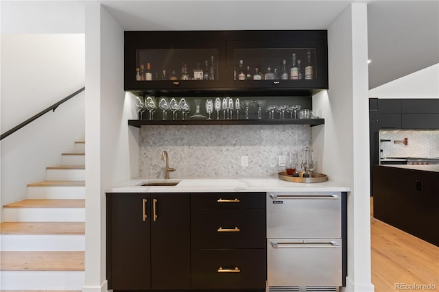 bar featuring tasteful backsplash, light wood-type flooring, stairs, indoor wet bar, and a sink