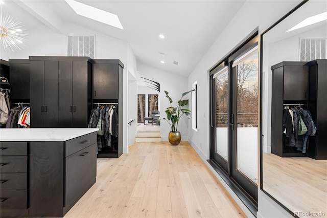 walk in closet with lofted ceiling with skylight, light wood-style floors, and visible vents