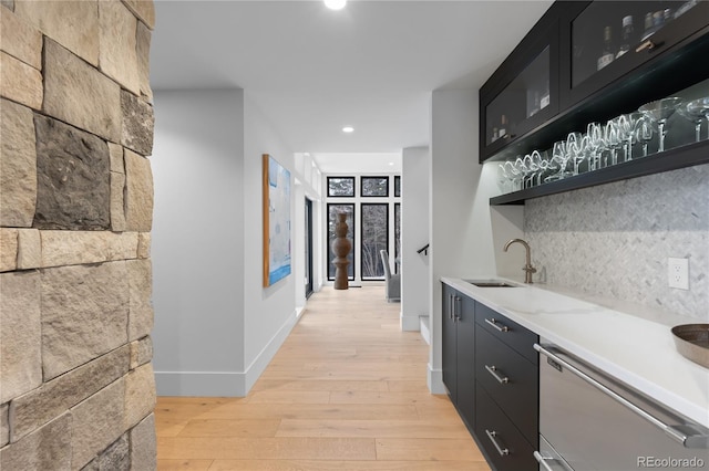 bar with dishwasher, decorative backsplash, light wood-style flooring, wet bar, and a sink