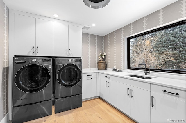 laundry area featuring independent washer and dryer, wallpapered walls, cabinet space, a sink, and light wood-type flooring