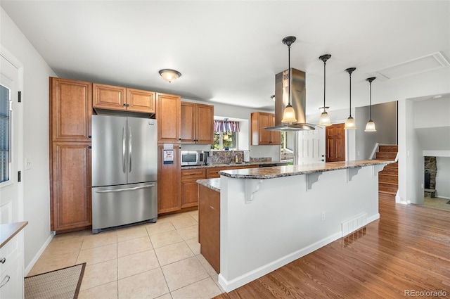 16225 W 74th Dr, Arvada, CO 80007 - kitchen with stainless steel appliances, island exhaust hood, a kitchen breakfast bar, brown cabinetry, and stone counters