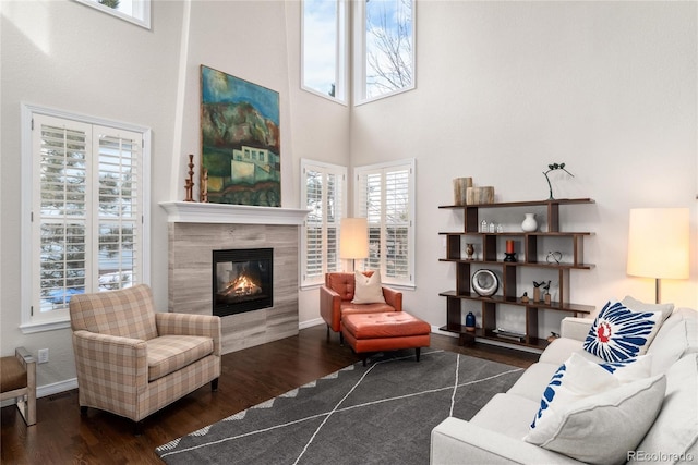 living area featuring dark wood-type flooring, a tile fireplace, a high ceiling, and baseboards