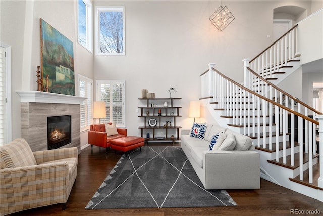 living room featuring a towering ceiling, stairway, dark wood finished floors, and a tiled fireplace