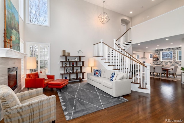 living room with a high ceiling, dark wood-style flooring, stairs, a glass covered fireplace, and an inviting chandelier