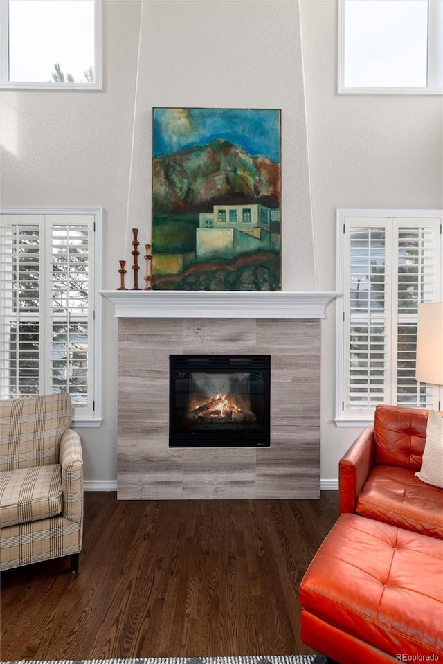 living room with plenty of natural light, dark wood-style flooring, a tiled fireplace, and baseboards