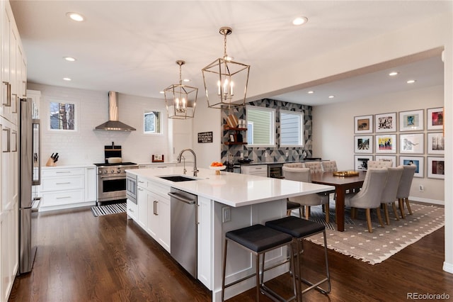 kitchen featuring white cabinets, wall chimney exhaust hood, stainless steel appliances, light countertops, and a sink