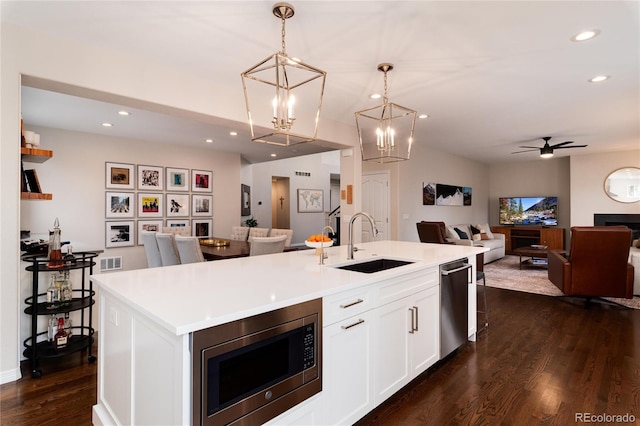 kitchen with stainless steel appliances, open floor plan, light countertops, a center island with sink, and pendant lighting