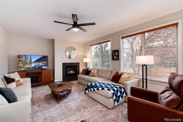 living room featuring wood finished floors, a glass covered fireplace, and a ceiling fan