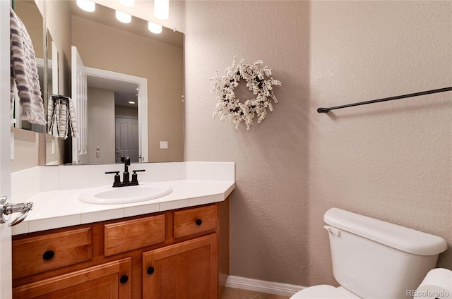 bathroom with a textured wall, vanity, and toilet