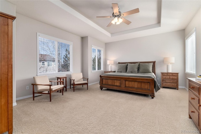 bedroom with light carpet, a tray ceiling, and baseboards