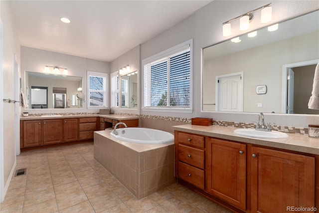 bathroom featuring a garden tub, two vanities, visible vents, a sink, and tile patterned flooring