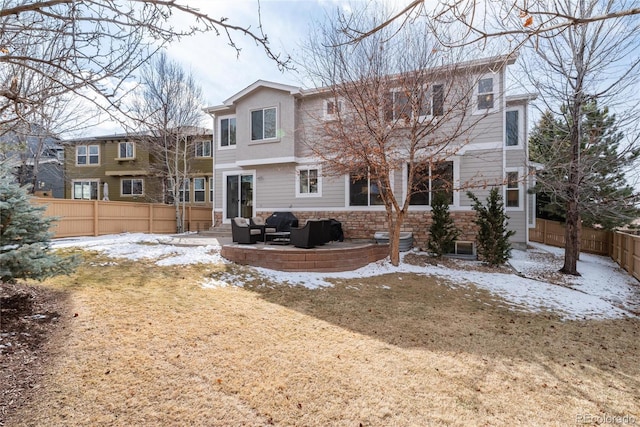 snow covered house featuring stone siding, a fenced backyard, and a yard