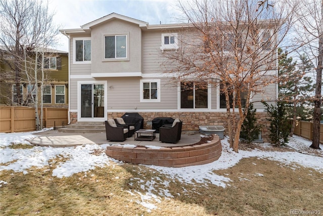 snow covered property with entry steps, stone siding, a patio area, and fence