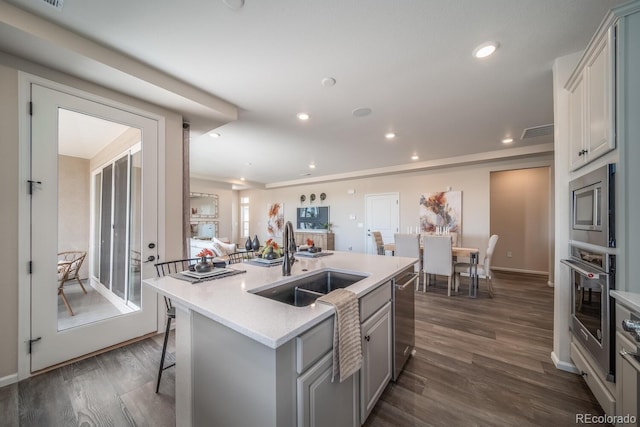 kitchen with sink, a kitchen breakfast bar, stainless steel appliances, an island with sink, and dark hardwood / wood-style flooring