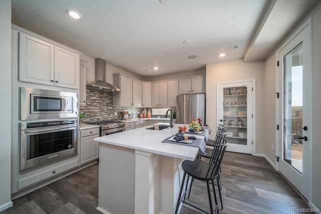 kitchen featuring sink, premium appliances, an island with sink, white cabinets, and wall chimney exhaust hood