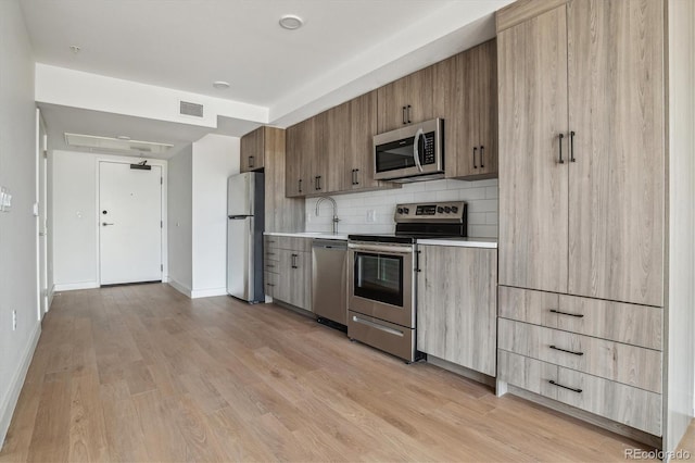 kitchen with decorative backsplash, stainless steel appliances, sink, and light hardwood / wood-style flooring