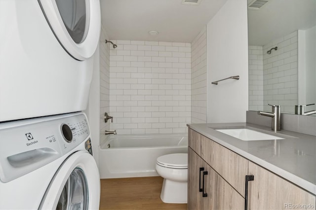 full bathroom with toilet, tiled shower / bath, vanity, stacked washer / dryer, and wood-type flooring