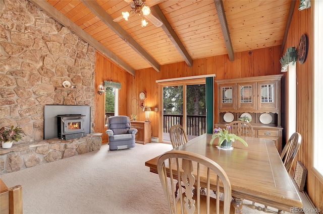 dining space with beamed ceiling, wooden walls, a wood stove, a baseboard radiator, and carpet flooring