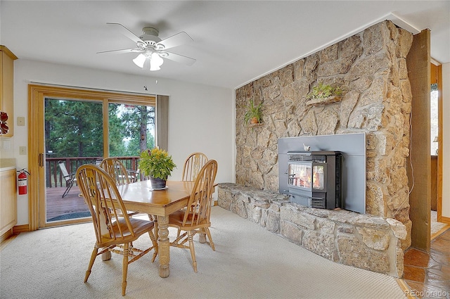 carpeted dining space with a wood stove, ceiling fan, and a stone fireplace