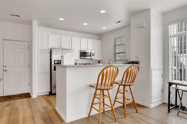 kitchen featuring white cabinets, kitchen peninsula, appliances with stainless steel finishes, and light hardwood / wood-style flooring