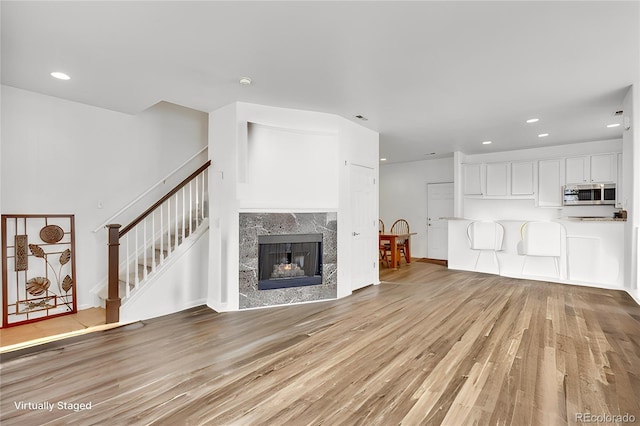 unfurnished living room featuring light wood-style flooring, recessed lighting, stairway, and a premium fireplace