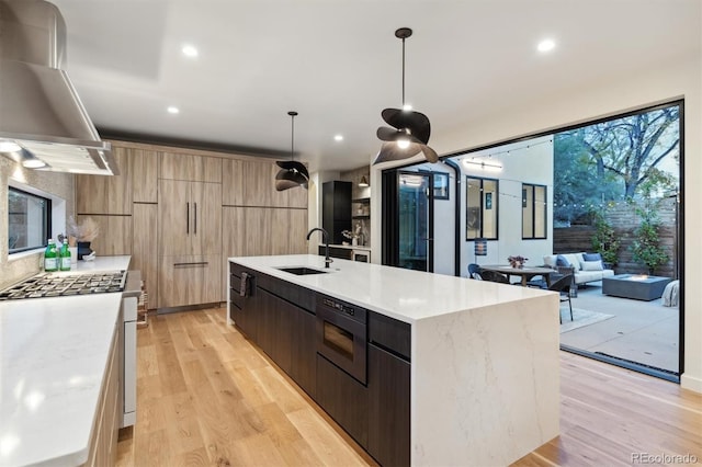 kitchen with hanging light fixtures, sink, wall chimney exhaust hood, and a spacious island