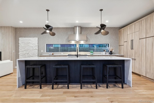 kitchen featuring sink, wall chimney exhaust hood, a spacious island, light brown cabinetry, and light wood-type flooring