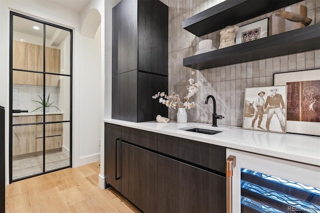 bar with sink, beverage cooler, tasteful backsplash, light hardwood / wood-style flooring, and dark brown cabinets