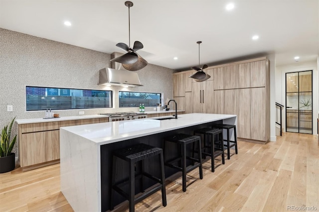 kitchen featuring a large island with sink, sink, hanging light fixtures, light hardwood / wood-style floors, and a breakfast bar area