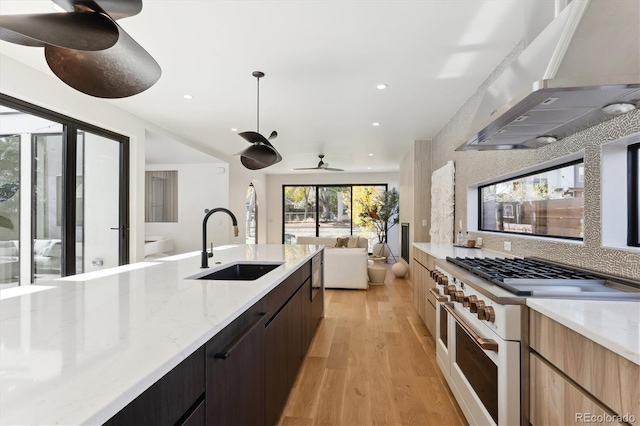 kitchen with light stone countertops, sink, wall chimney range hood, high end stainless steel range, and light hardwood / wood-style floors