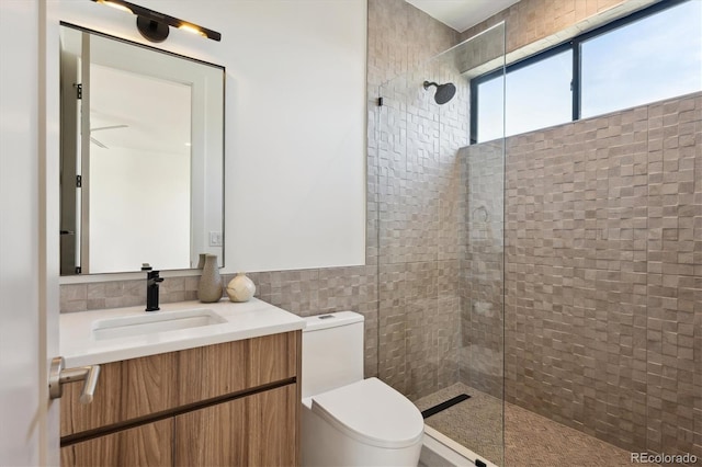 bathroom featuring vanity, toilet, a shower with shower door, and tile walls