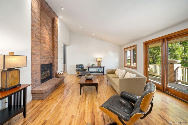 living room with light hardwood / wood-style floors, high vaulted ceiling, and a brick fireplace