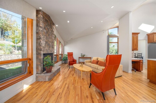 living room with high vaulted ceiling, a stone fireplace, and light wood-type flooring