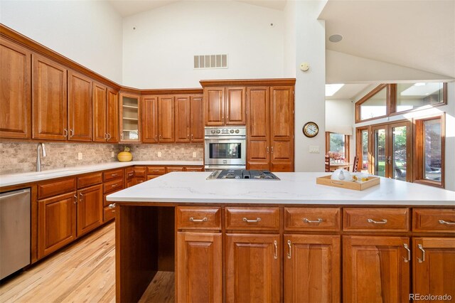 kitchen featuring stainless steel appliances, backsplash, a center island, light wood-type flooring, and high vaulted ceiling