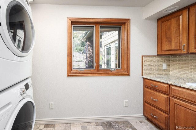 washroom with stacked washer and clothes dryer, light hardwood / wood-style floors, and cabinets