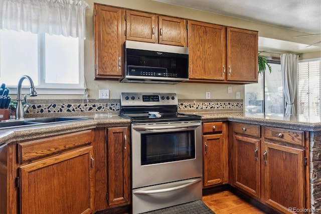 kitchen featuring a sink, brown cabinets, stainless steel range with electric stovetop, and light wood-style flooring