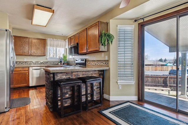 kitchen featuring stainless steel appliances, a peninsula, dark wood finished floors, and brown cabinetry