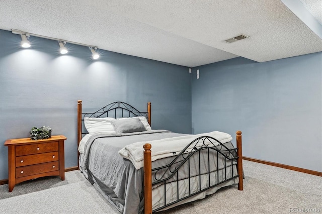 carpeted bedroom featuring visible vents, rail lighting, a textured ceiling, and baseboards