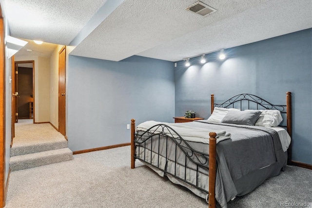 carpeted bedroom featuring visible vents, a textured ceiling, track lighting, and baseboards