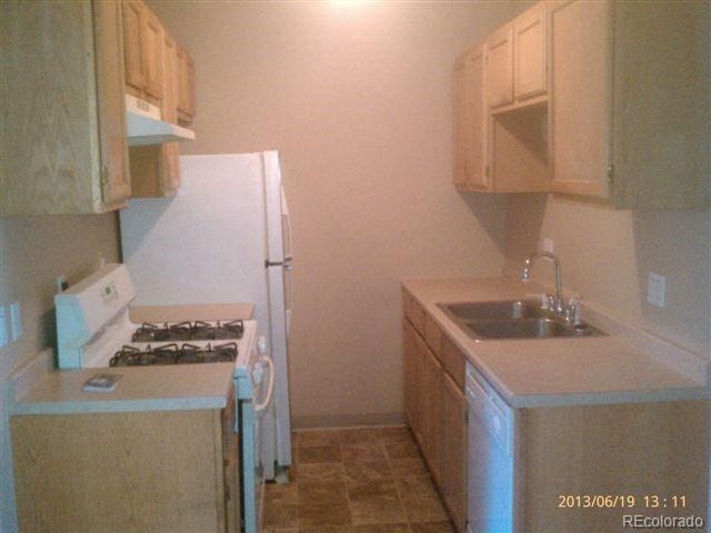 kitchen featuring white appliances, under cabinet range hood, a sink, and light countertops