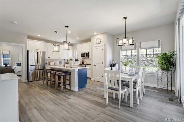 16277 Talons Bluff Ln, Monument, CO 80132 - kitchen featuring appliances with stainless steel finishes, a chandelier, light countertops, an island with sink, and light wood-type flooring