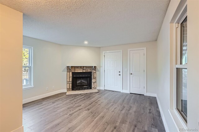 unfurnished living room with a textured ceiling, a stone fireplace, wood finished floors, and baseboards