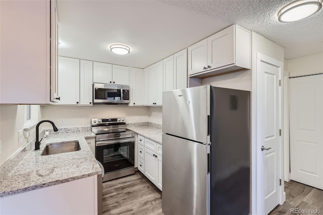 kitchen featuring stainless steel appliances, a sink, light wood-style flooring, and white cabinets